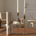 Gold candle holders with white candles on a wooden table, next to a white box with a brown ribbon.