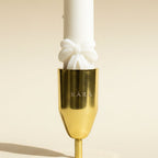 Gold candle holder with a white candle on a beige background, featuring the brand 'KARA'.