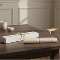 White gift box with candles with a bow on a wooden table, with white bowls in the background.