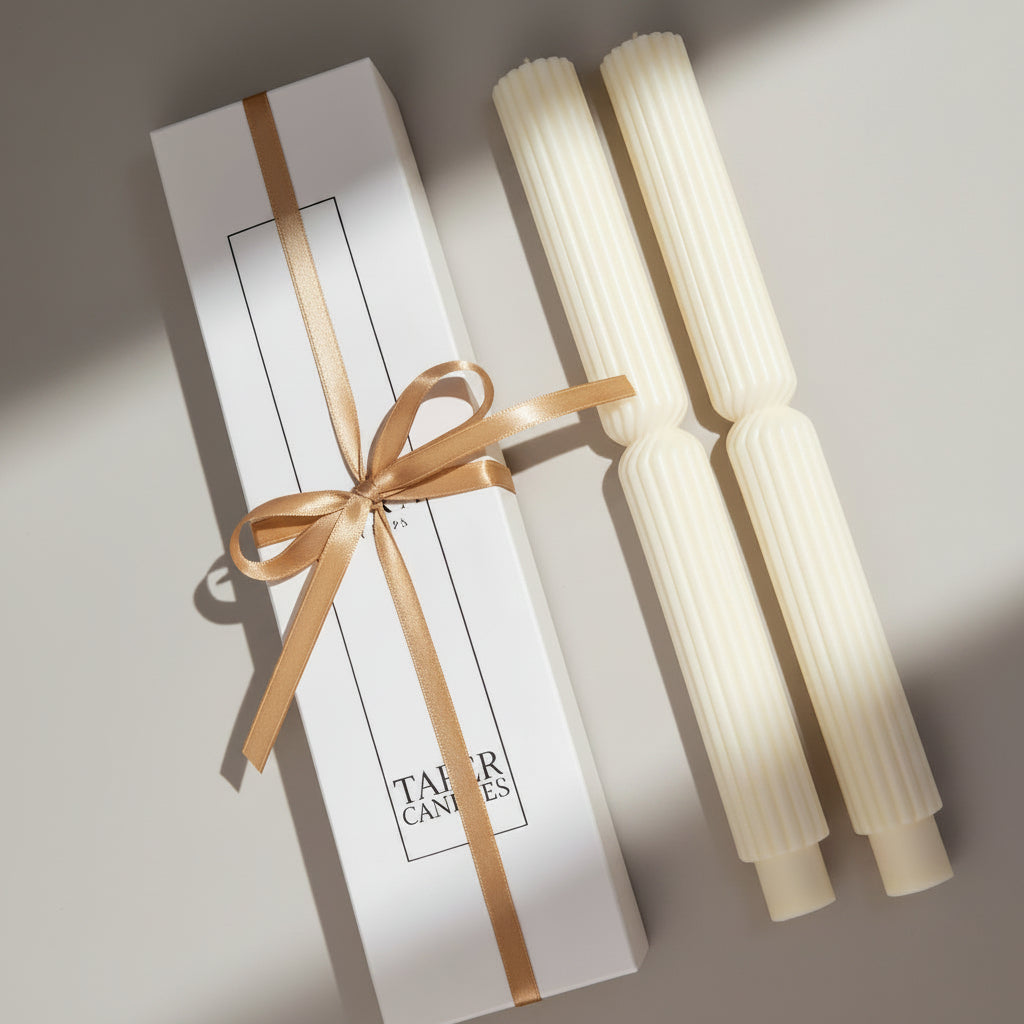 Two white taper candles with a gold bow on a white box