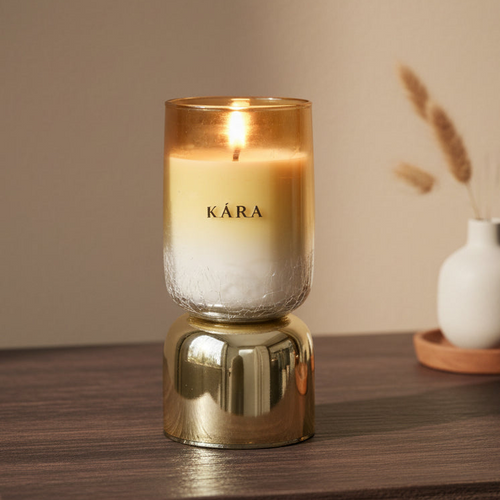 Candle in a glass holder with KÁRA branding on a wooden surface.