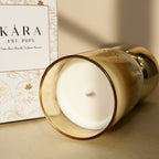 Gold candle holder with a white candle inside, KÁRA brand visible in the background.