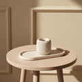 Round beige table with a textured white candle and matching tray against a beige wall.