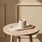 Round beige table with a textured white candle and matching tray against a beige wall.
